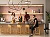 Group of residents gathered around a kitchen island, chatting and preparing food in a stylish, modern communal space with decorative lighting and shelves in the background