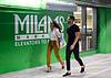 Two people walking past a brightly lit at Milam's Market sign, smiling and enjoying their time together