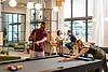 Residents playing pool in lounge area, with modern seating, large windows, and stylish lighting in the background