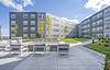 Apartment building courtyard with chairs and sitting area.  Sunny day with trees, grass and blue skys.