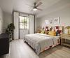 A colorful modern bedroom featuring a patterned headboard, large windows, curtains, a plant, and stylish lighting.