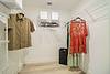 A walk-in closet with hanging clothes, including a red lace dress and various shirts, plus storage boxes and a bin.
