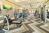 A modern gym with exercise machines, weights, and a television on the wall, featuring a stylish carpet design.