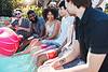 Group of friends enjoying a pool party, sitting on the edge, holding red cups, with a large inflatable ball in the water.