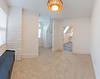 Bright, empty room with beige carpet, large windows, and a decorative light fixture. White walls and a corner fireplace.