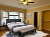 A cozy, well-lit bedroom with a bed, bench, nightstand, and large windows featuring yellow walls and wooden floors.