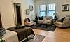 A cozy living room with a sofa, armchair, coffee table, and decorative accents, featuring natural light from windows.