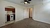 A spacious living area with carpet, a ceiling fan, and an adjoining kitchen with brown cabinets and white appliances.