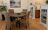 A cozy dining area featuring a round table, four woven chairs, a decorative bowl, and a cabinet with glass doors.