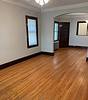 A spacious, empty living room with hardwood floors, light gray walls, and two windows, featuring an archway and a mirror.