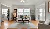 Bright living room with a white sofa, coffee table, decorative pillows, plants, and natural light from large windows.