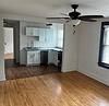 A bright living area with hardwood floors, a ceiling fan, and an open kitchen featuring white cabinets and appliances.