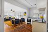 Bright living room with blue sofas, a yellow rug, and a kitchen area featuring a sink and stove, abundant natural light.