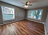 A bright room with wooden floors, a ceiling fan, air conditioner, and large windows letting in natural light.