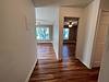 A hallway with hardwood floors, leading to a living area with windows and a doorway on the right.