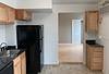 A modern kitchen with wooden cabinets, a black refrigerator, and an open layout leading to a light-colored room beyond.