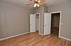 A room with light brown wooden floors, gray walls, a ceiling fan, and open closet doors.