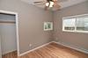 A small, empty bedroom with light wood flooring, a ceiling fan, and a window, featuring a closet on one side.