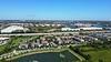 Aerial view of a suburban area featuring homes, a pond, roads, and waterways under a clear blue sky.