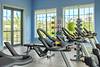 A fitness room with stationary bikes, exercise equipment, and large windows providing natural light.