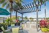 Outdoor grilling area with a pergola, barbecue grills, a table, and tropical plants under a clear blue sky.
