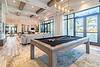 A bright living space featuring a pool table, modern furniture, and large windows overlooking a pool area.