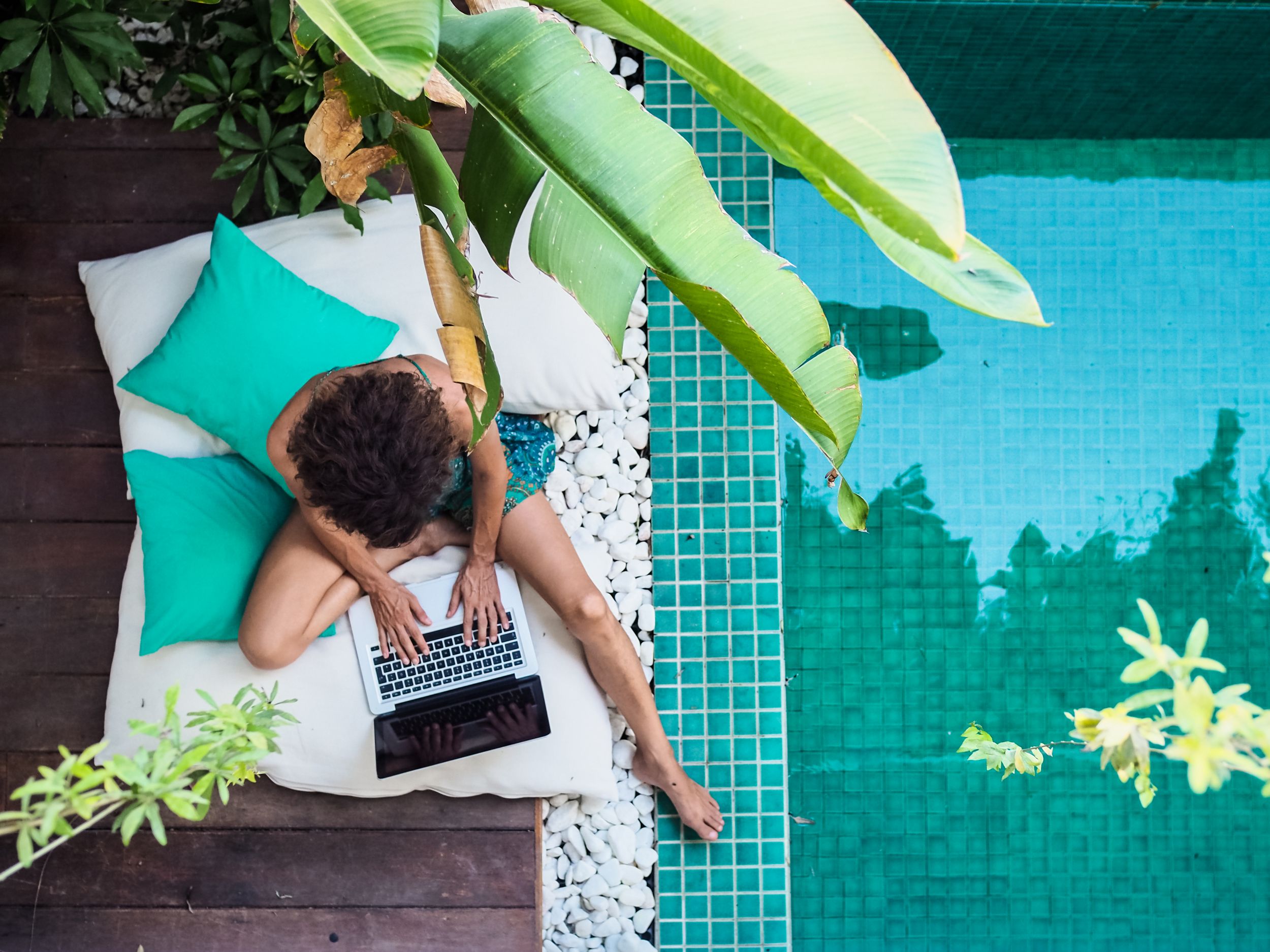 Woman using laptop on deck next to pool