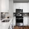 Kitchen with white cabinetry, white quartz countertops, tile backsplash, stainless steel appliances, and hard surface flooring