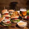 a table full of burgers and a glass of beer