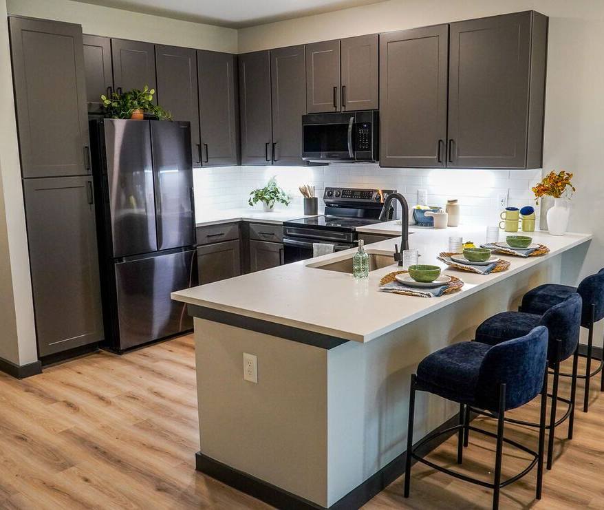 A modern kitchen featuring dark cabinets, stainless steel appliances, a large island, and stylish bar stools.