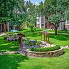 A well-maintained lawn with trees, pathways, and a seating area featuring pergolas in an apartment complex.