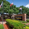 A welcoming sign for Park West, surrounded by greenery and flags, under a clear blue sky.