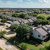 Aerial view of a residential neighborhood with houses, green lawns, and parking areas under a blue sky.