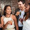 Four friends enjoying drinks and laughing together in a social setting with a brick background.