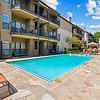 Swimming pool surrounded by lounge chairs, landscaped area, and apartment buildings under a clear blue sky.