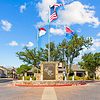 Stone sign for Hidden Ray Apartments with U.S. and Texas flags, surrounded by trees and clear blue sky.