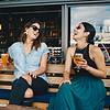 Women laughing and drinking beer on bench outside