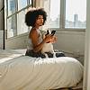 Woman using smartphone on bed with dog on lap