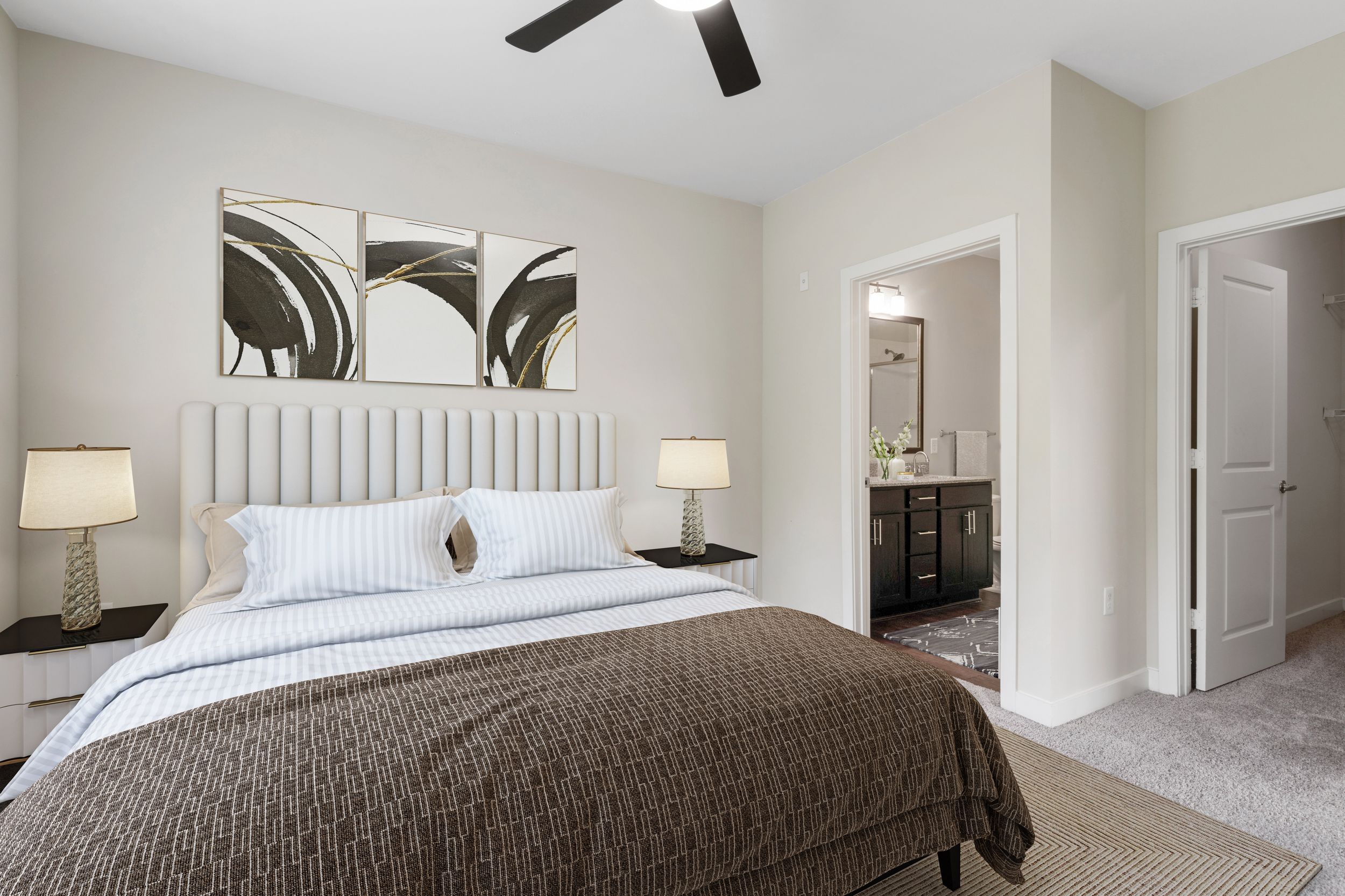 Master bedroom with plush carpet, modern ceiling fan, spacious walk-in closet, and en suite bathroom at Realm at Patterson Place by Lantower Residential.
