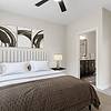 Bedroom with tan carpet, a ceiling fan, 9-foot ceilings, large windows, a large, cream bed with brown bedding and modern wall art at Realm at Patterson Place Apartments.