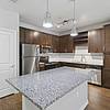 An apartment's kitchen with granite counters, wood plank floors, espresso custom cabinetry, stainless steel, energy efficient appliances, and tile backsplash at Lantower Asturia.