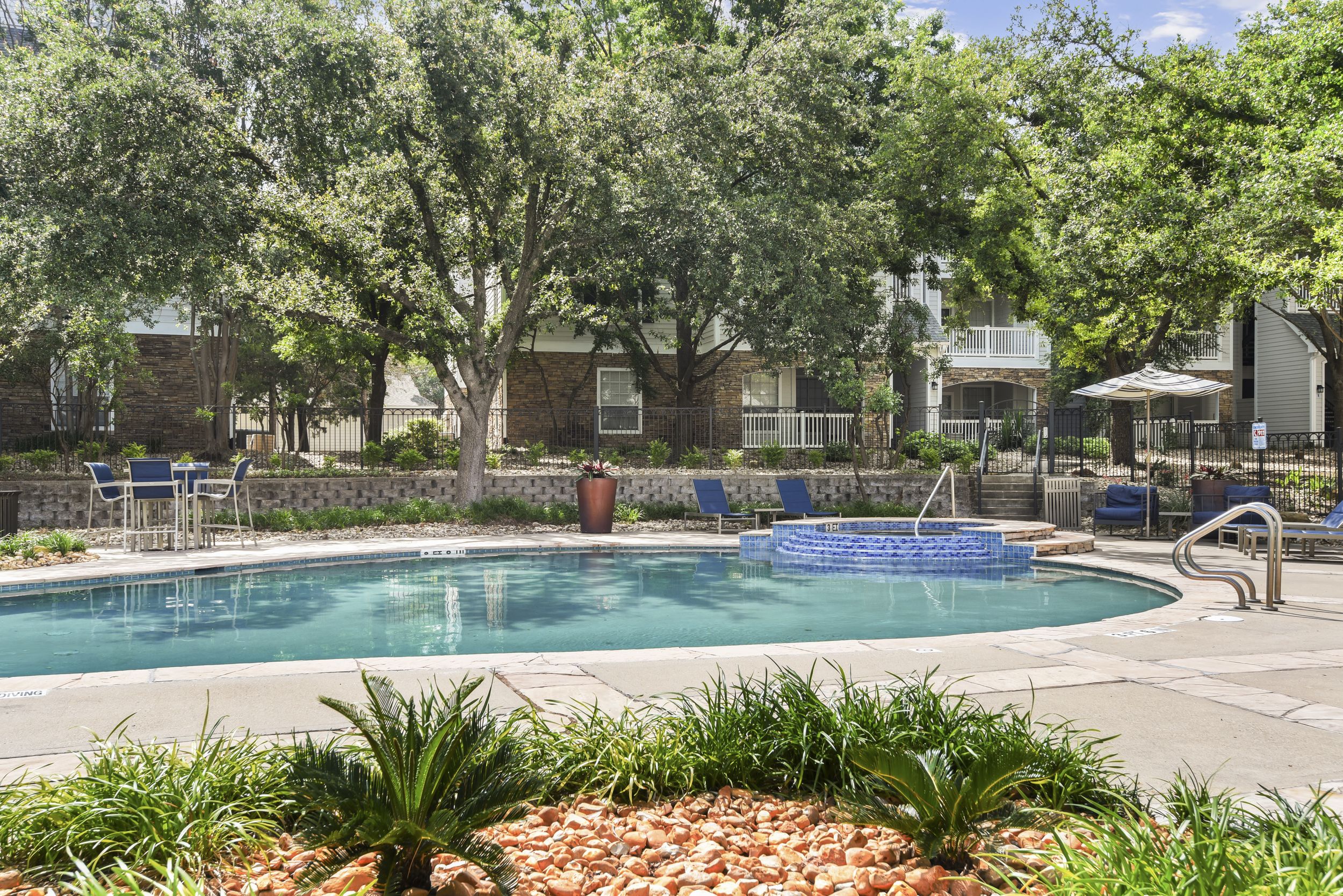 Classic swimming pool area with outdoor seating, pool umbrellas, and a hot tub at Lantower Round Rock.