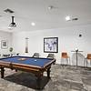 Room with stone flooring, a wood-style accented pool table, elevated tables accompanied by stools, and a large projector screen on the wall at Lantower Round Rock