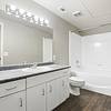 Modern bathroom with ample lighting, A large, well lit mirror, and finished with glossy shower tiling, and quartz countertops at Lantower Round Rock.