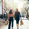 Two women walking away from the camera laughing and holding brown shopping bags