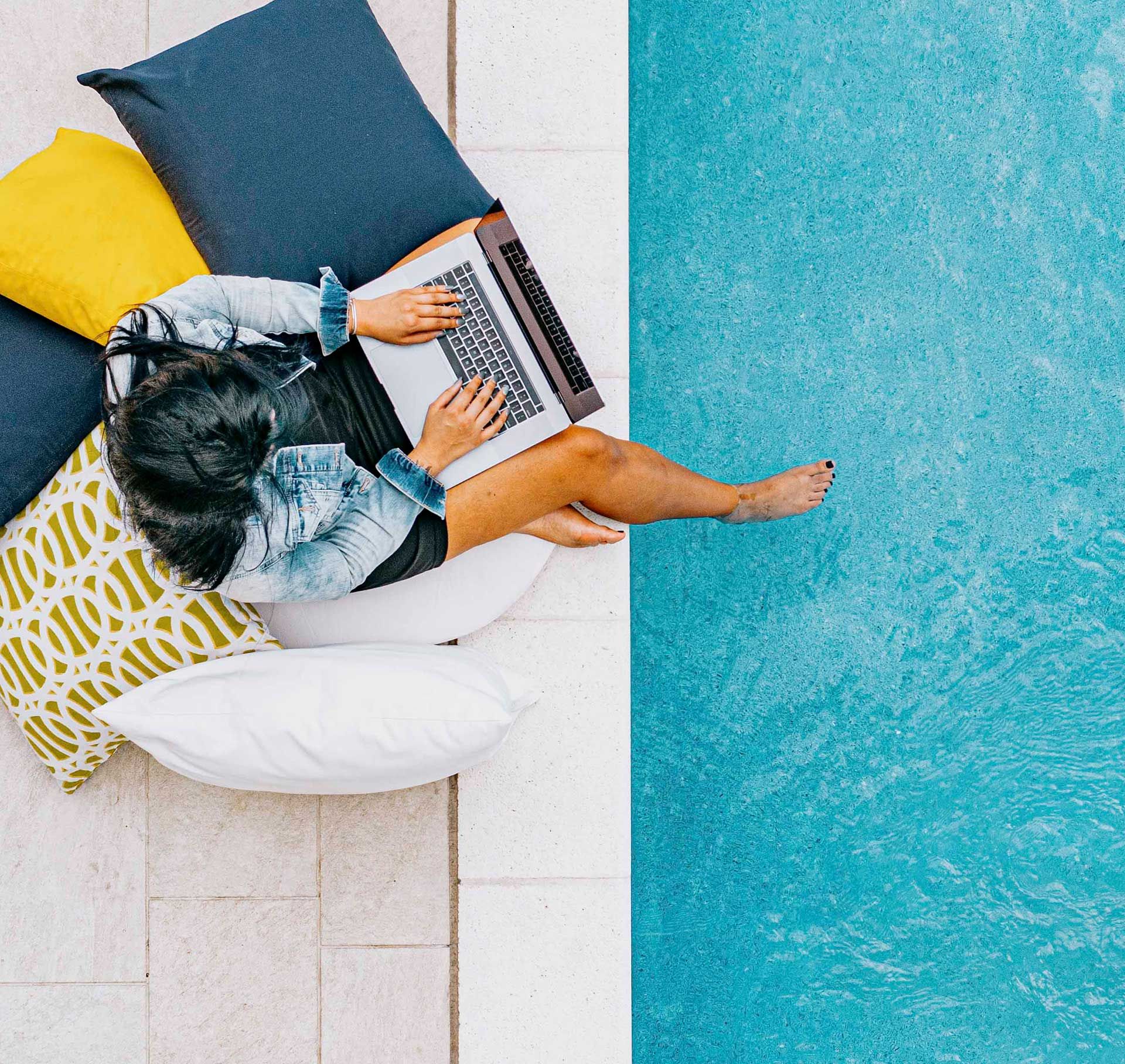 Woman sitting next to pool with laptop