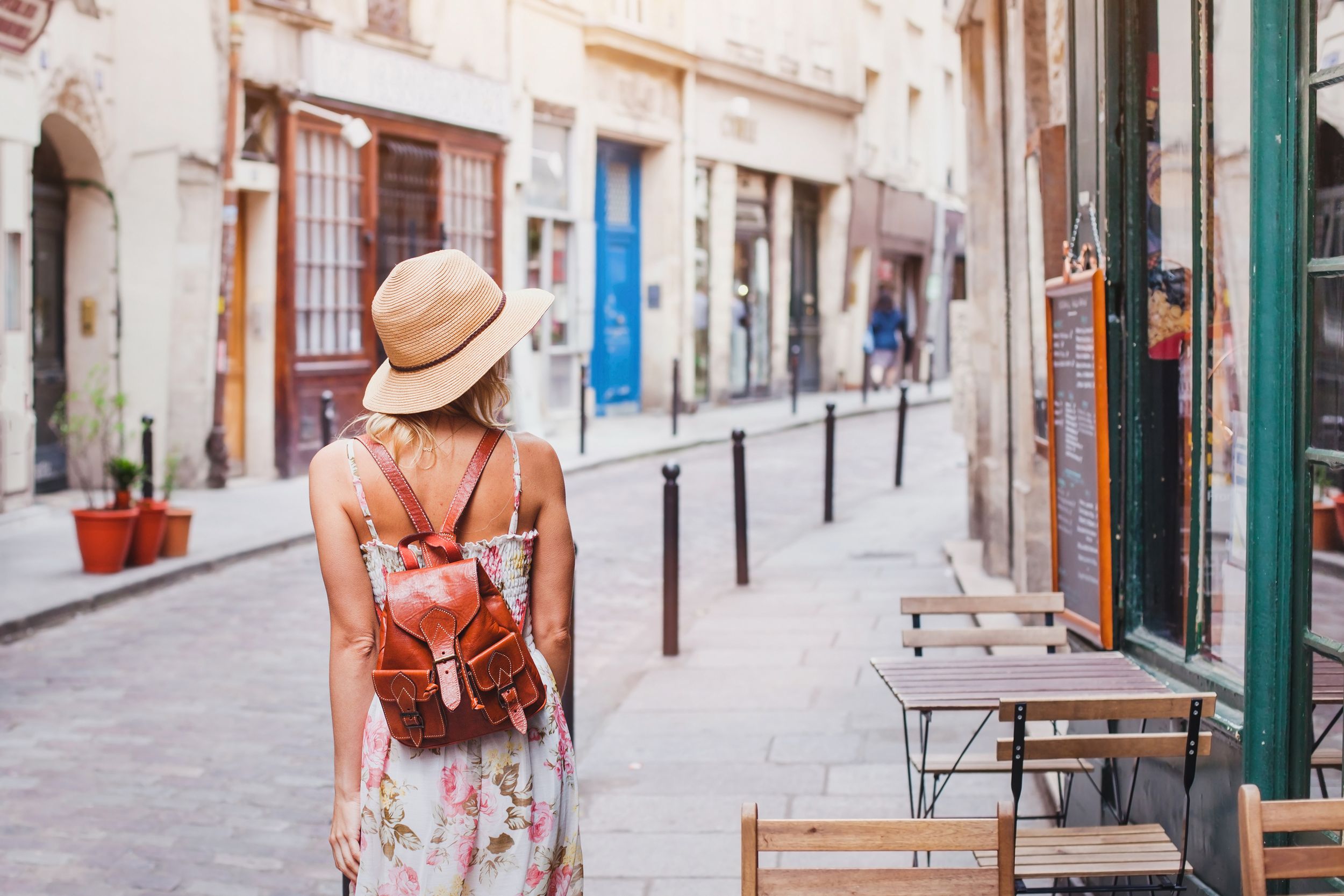 Woman walking down street next to shop with tables outside