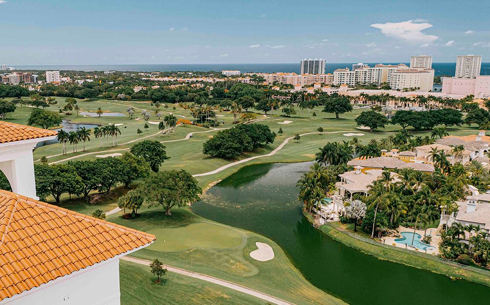 Aerial view of golf course with buildings and water in background