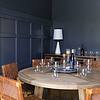 Round wooden table with wine glasses on it in a room with dark gray walls