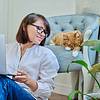 Woman on laptop next to cat in chair